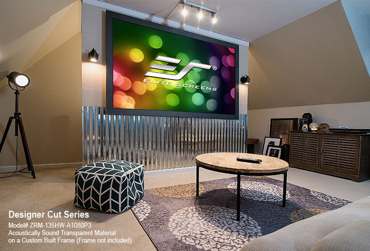 An indoor home cinema setup featuring a large projection screen with a colorful display, surrounded by a silver frame. The room has low lighting with spotlights and a coffee table in the foreground.