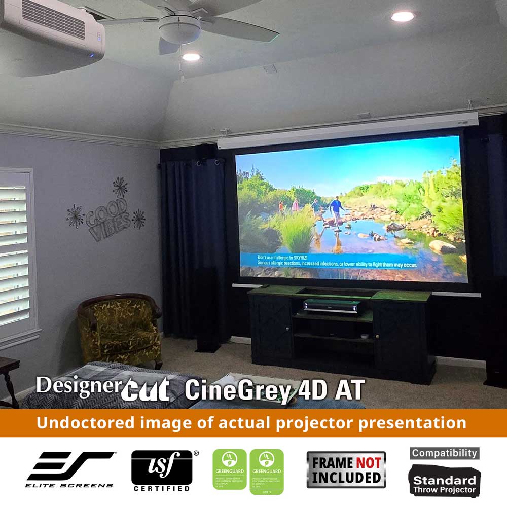 A home theater setup showing a large projector screen mounted on the wall, displaying a colorful video scene. The room has dark curtains, a ceiling fan, recessed lights, and a media console beneath the screen.