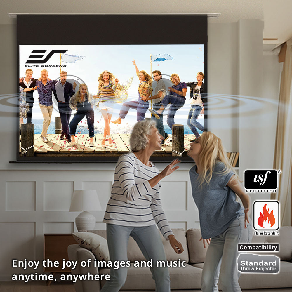 Two women dancing in a living room with a large screen displaying a family on a dock.