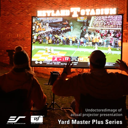 Two people watching a sports game projected onto a screen outdoors with 'Elite Screens' and 'TSF Certified' logos.